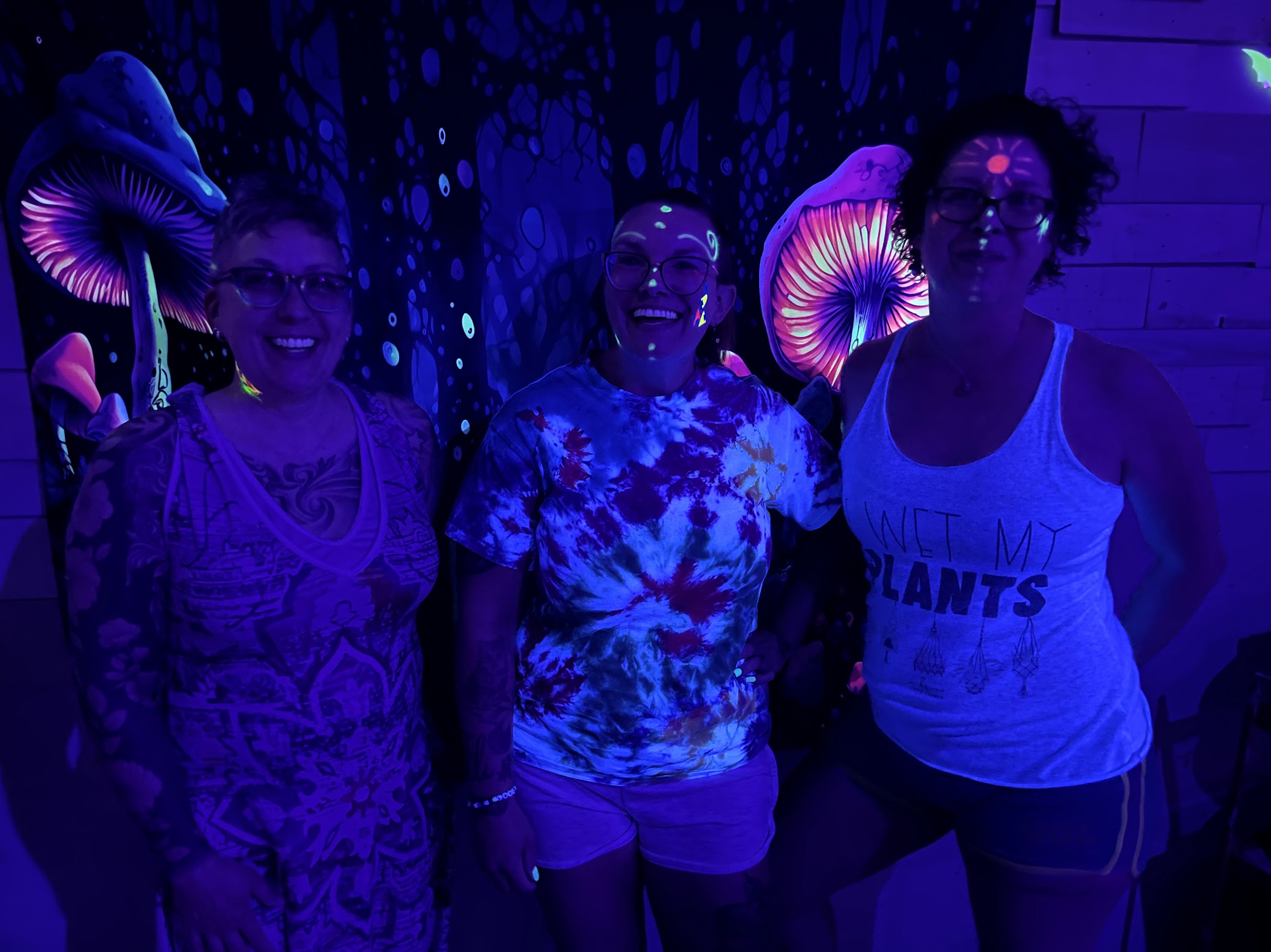 3 women with blacklight paint on their faces and arms posing for a picture in our black light pottery studio