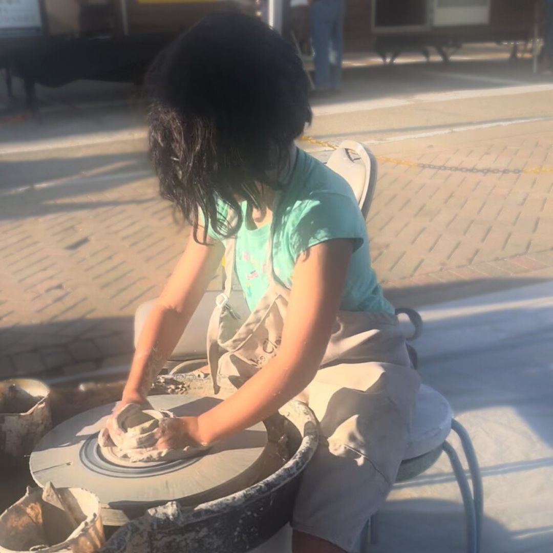 8 year old girl forms a bowl out of clay on a pottery wheel in downtown port huron during blue water fest at Foundry's demo tent