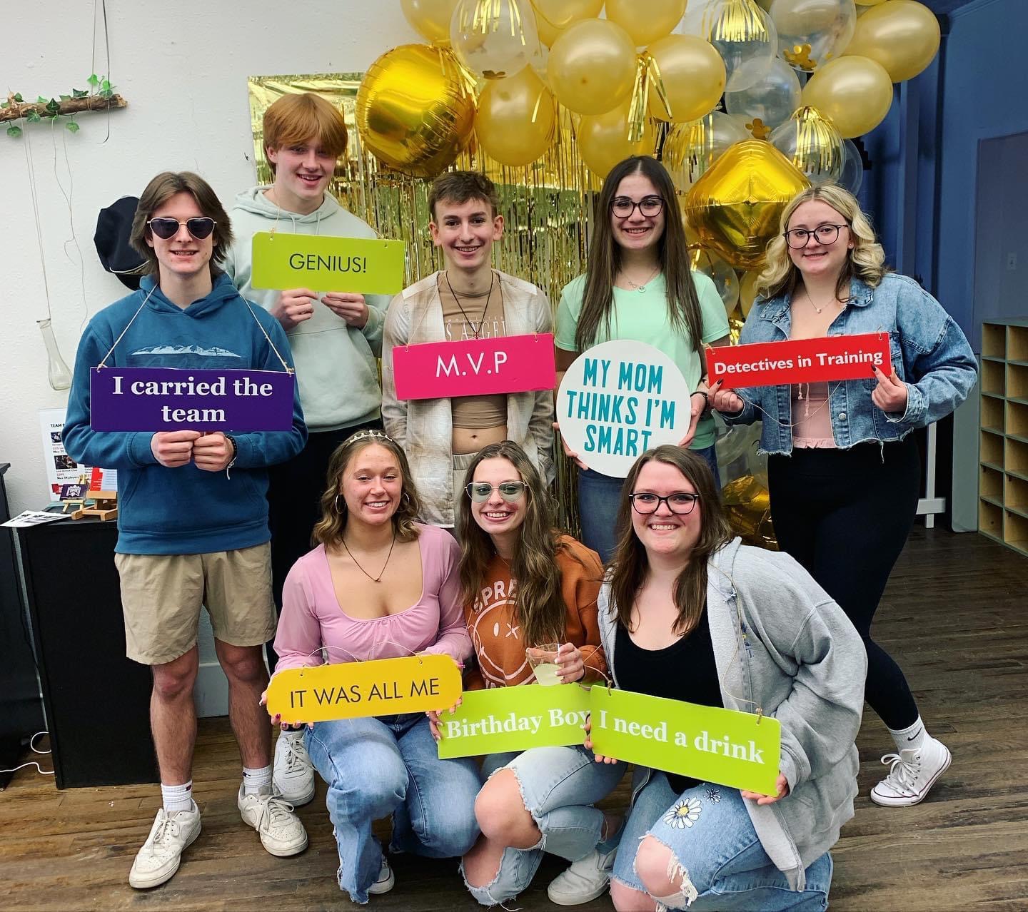 group of 8 high schoolers hold signs after completing an escape room at The Hallway Entertainment in Foundry