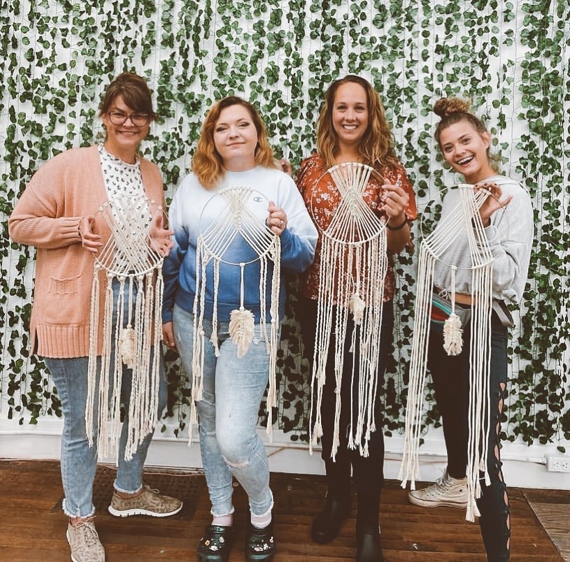group of four women holding up their macrame wall hangings after a macrame class at Foundry in Port Huron