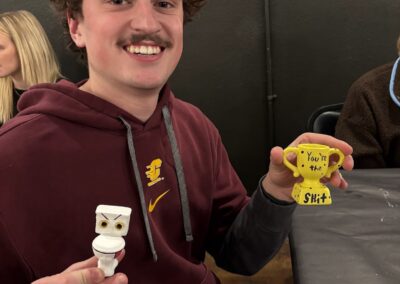 customer at art bar showing off two painted ceramics, one a toilet with googly eyes, the other a trophy.